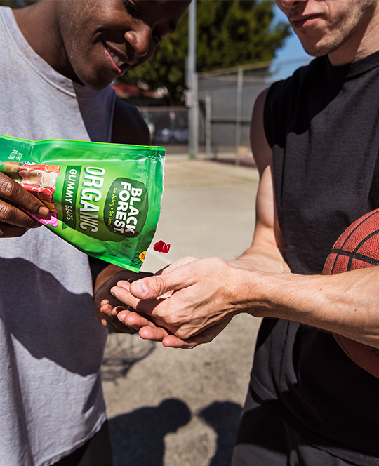 Two guys sharing gummy bears on a basketball court