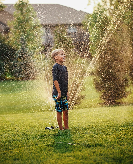 Kid standing on lawn with sprinkler
